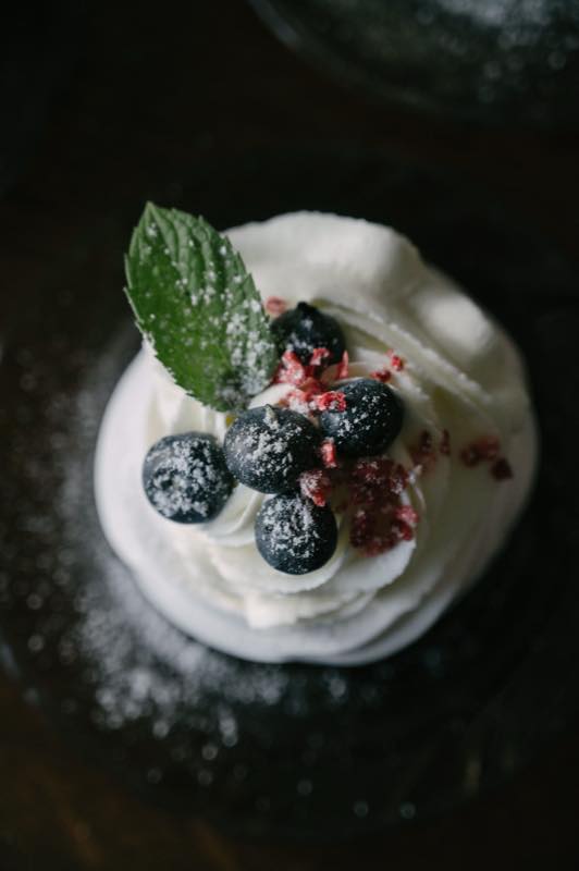 A pavlova topped with cream and winter berries