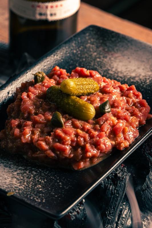 Steak tartare on a dark plate with cornichons and capers