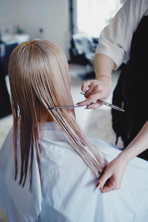 A stylist cutting long blonde hair, seen from behind