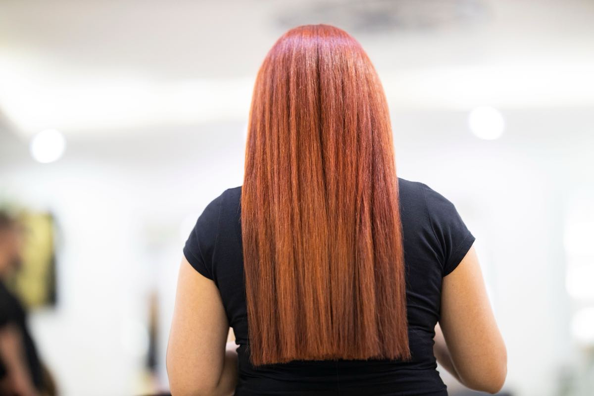 A client with long copper hair seen from behind in a bright salon