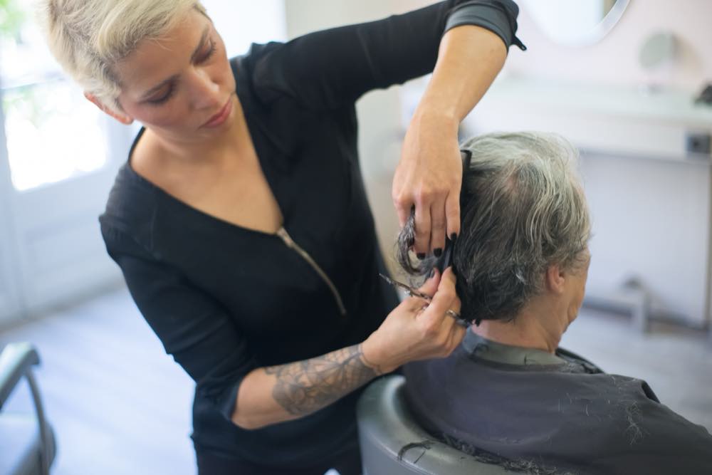 A stylist working on a client's hair beside a bright window