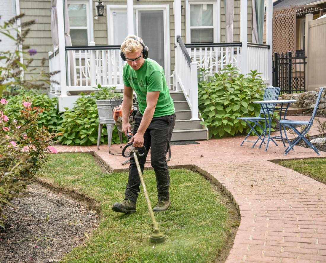 A landscaper edging a front lawn beside a brick path